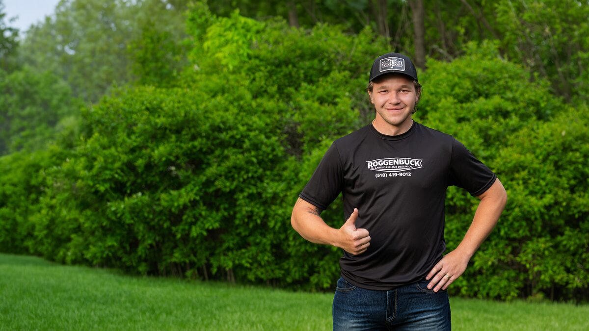 Mitchell Roggenbuck giving a thumbs up on a green lawn in front of a hedge